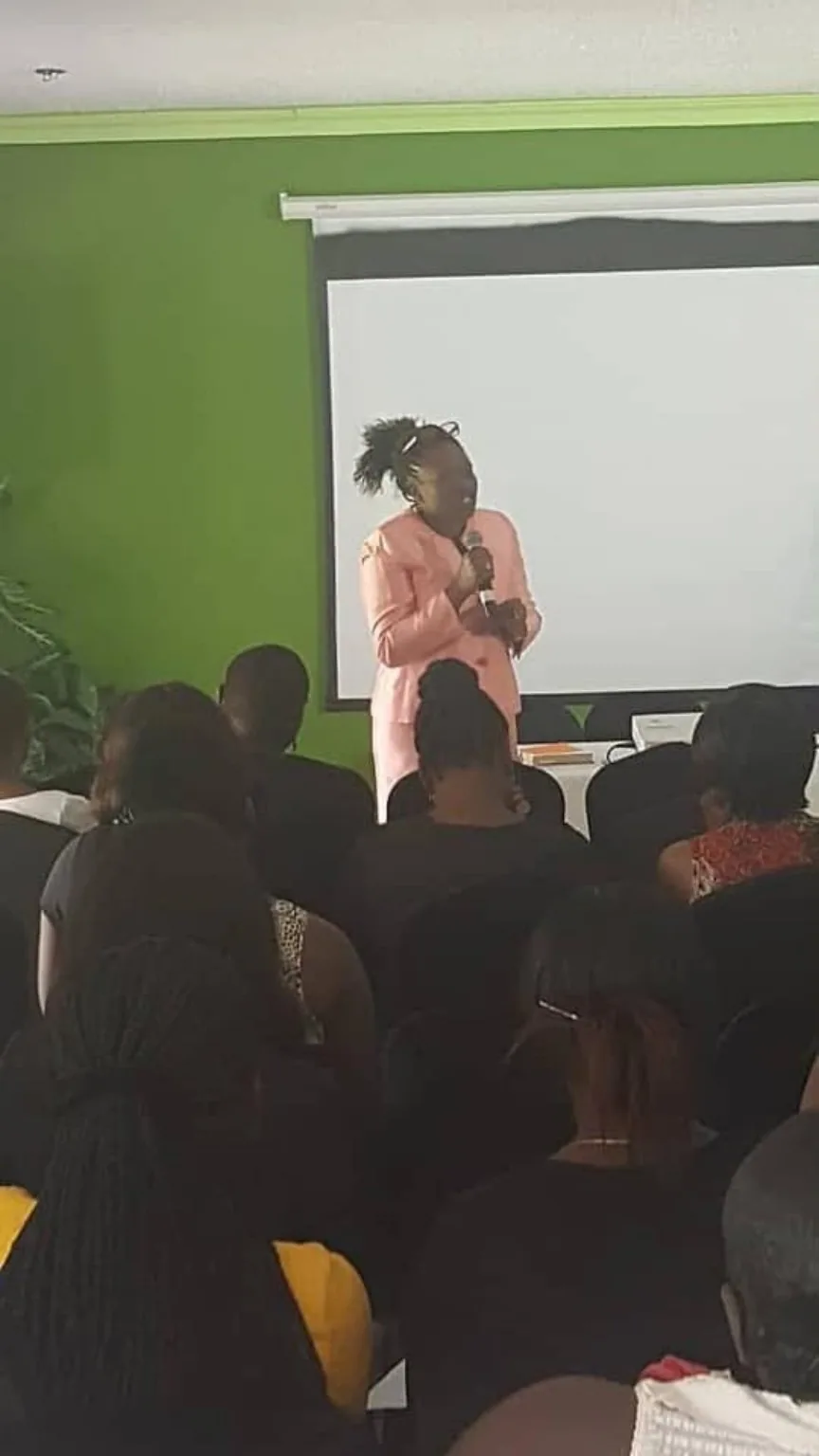 A facilitator in a pink suit speaks to an adult audience