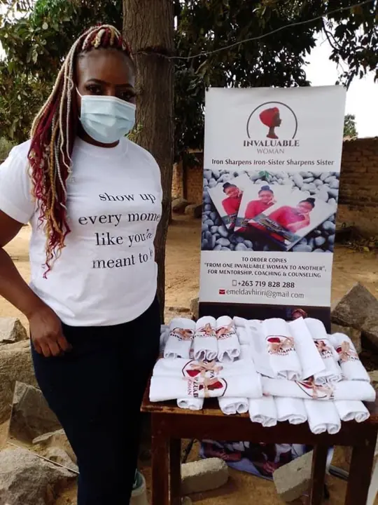 A woman stands beside Invaluable Woman materials during an outreach.
