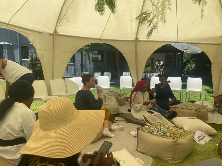 Women seated on cushions beneath a marquee.