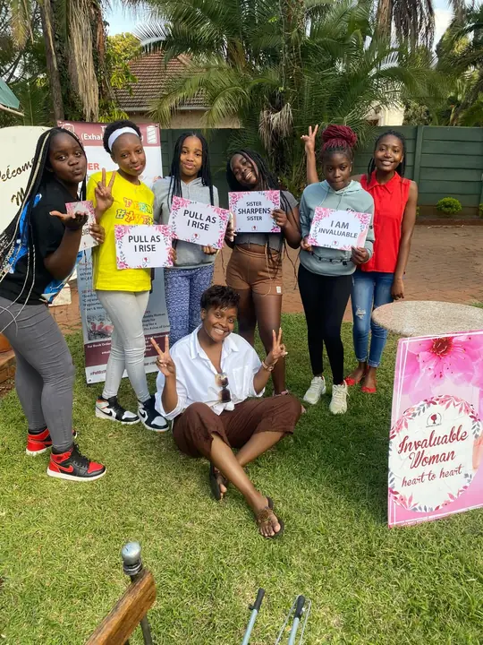 Young women hold signs reading Pull As I Rise, Sister Sharpens Sister and I Am Invaluable.
